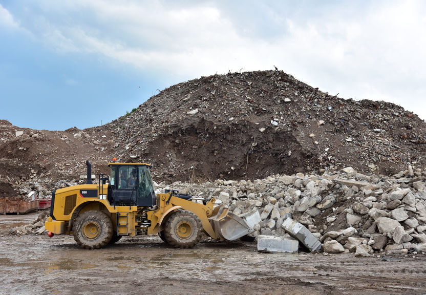 A yellow front loader moves debris and rocks in front of a large pile of rubble at a construction site.